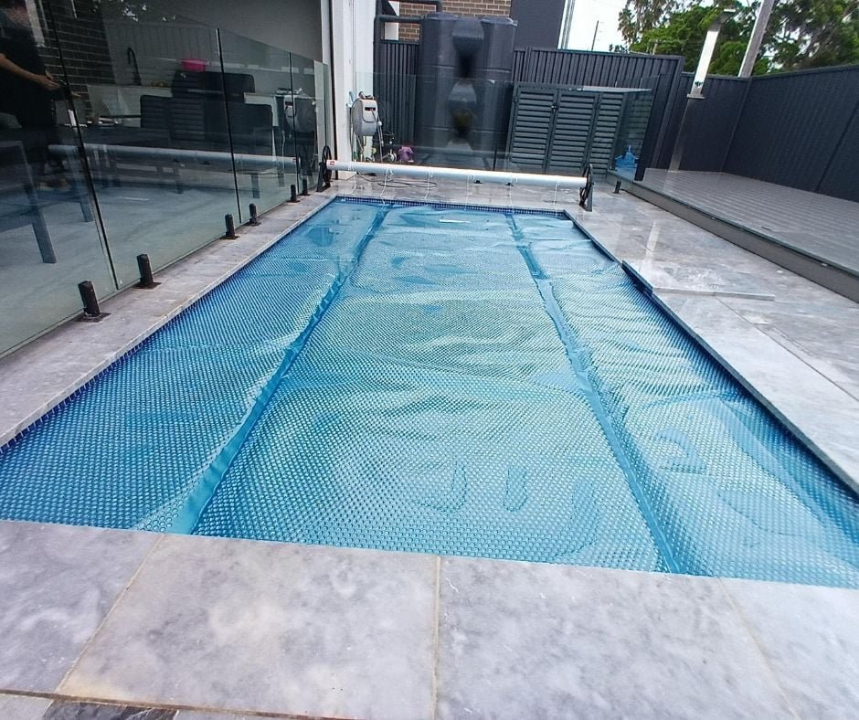 Blue solar pool cover fitted to a residential swimming pool with roller